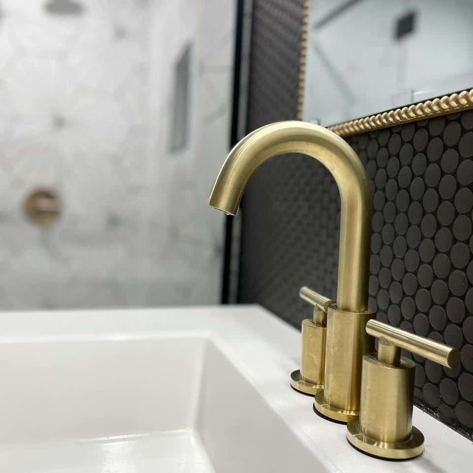 Close-up of a gold bathroom faucet with black tile and white sink