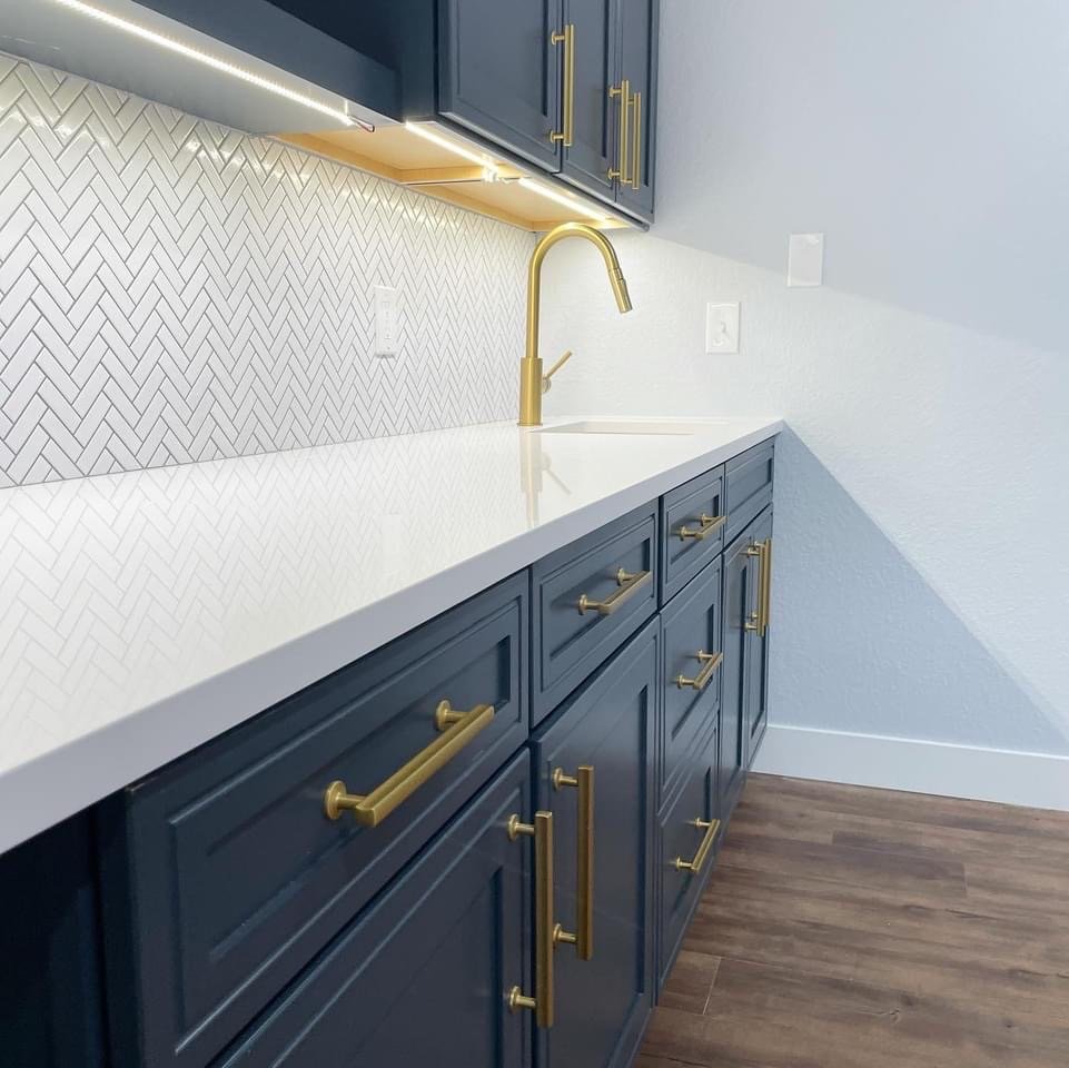 Wet bar with dark blue cabinets, gold hardware, and white counter top
