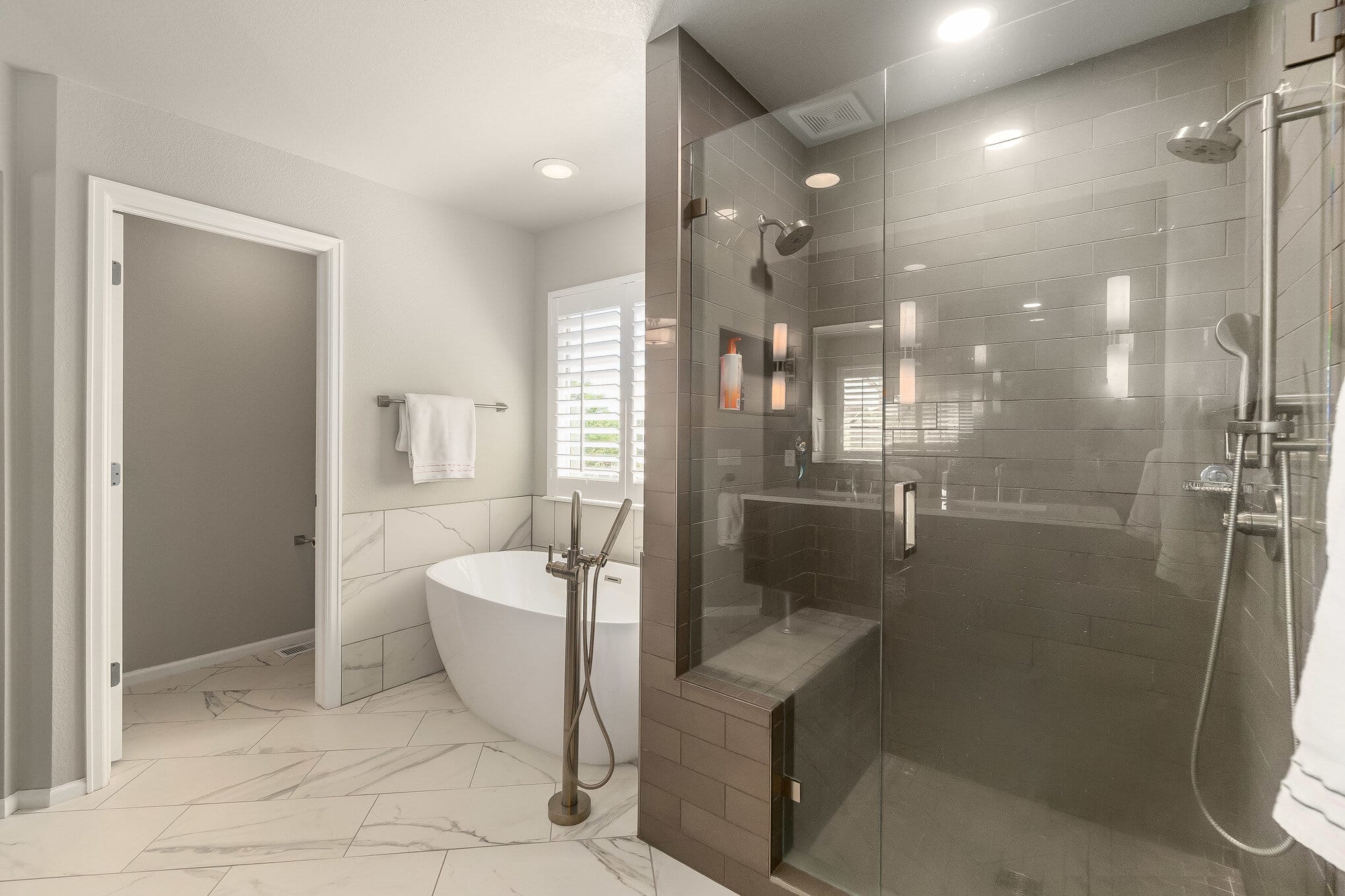 Large walk-in shower with dark tile and separate white tub on marble floor