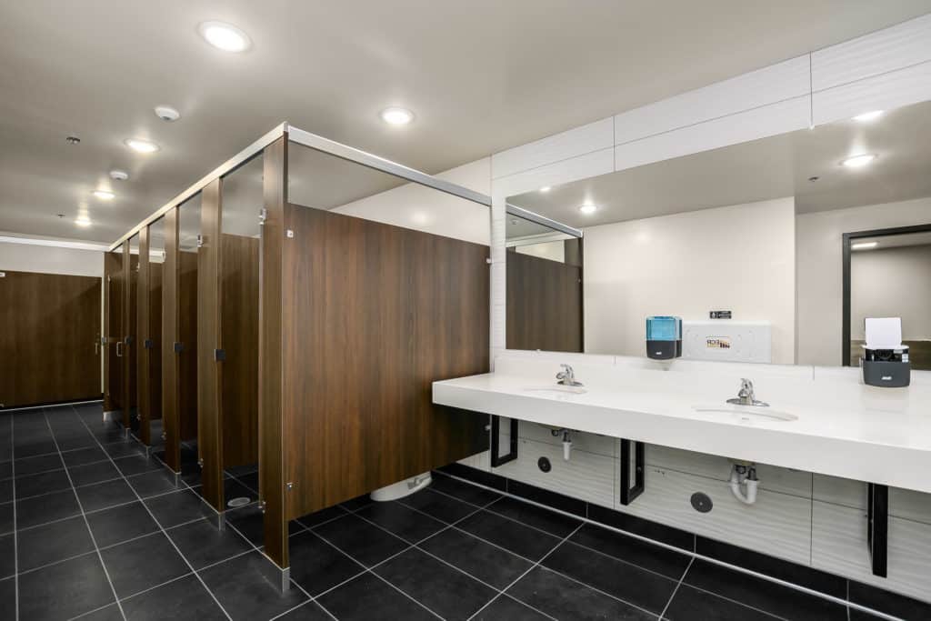 Public restroom with dark wood stalls, black tile floor, and white walls and sinks