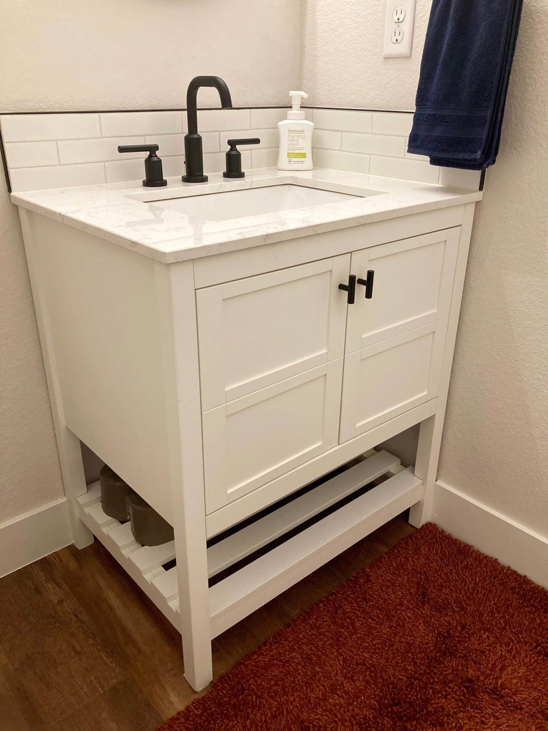 Half bathroom vanity with white subway tile and black faucet