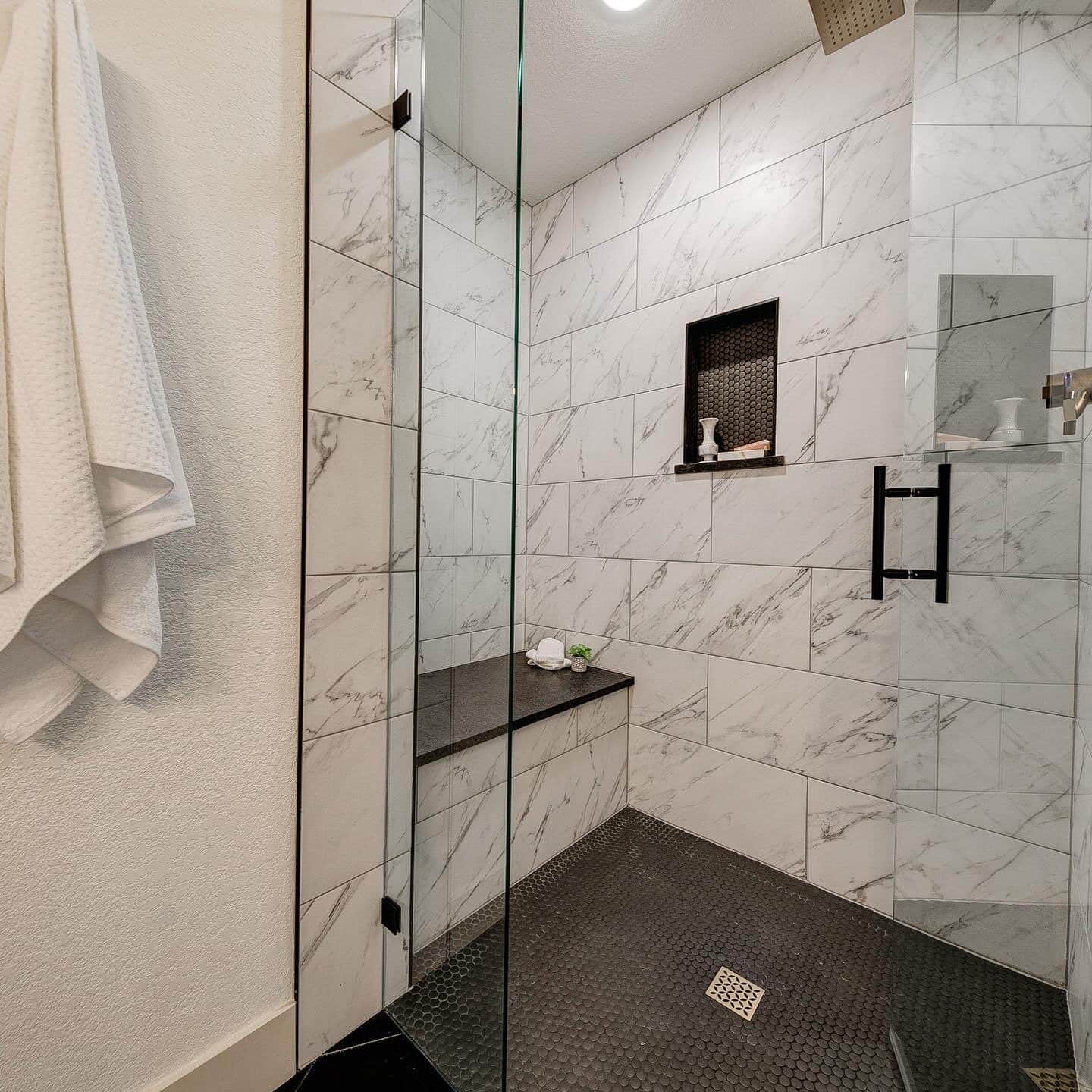 Large glassed-in shower with white marble tile walls and dark tile floor