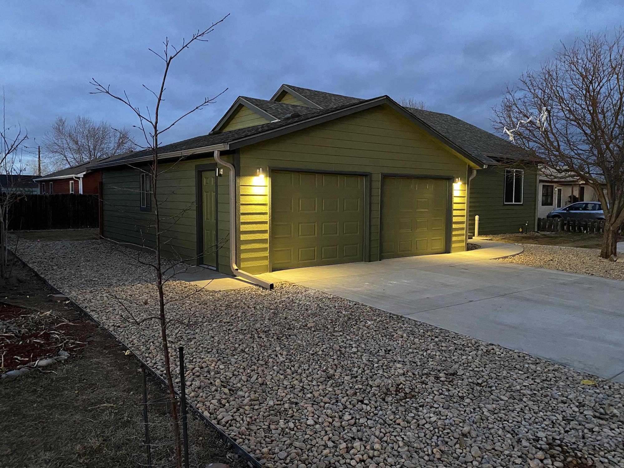 Corner view of a two-car garage with green siding and lights at night